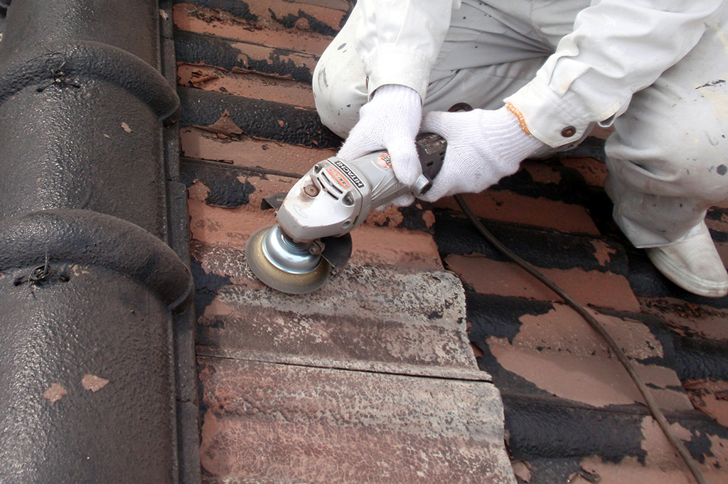 モニエル瓦屋根の旧塗膜をディスクサンダーで取り除いています。